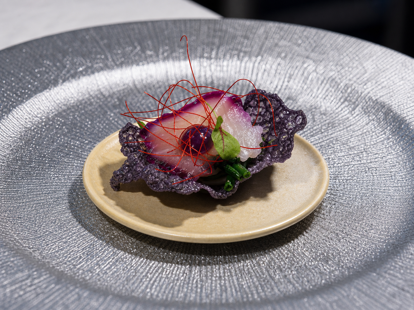 Piatto con cialda viola, crema chiara e fili rossi