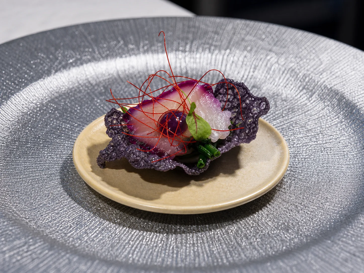 Piatto con cialda viola, crema chiara e fili rossi